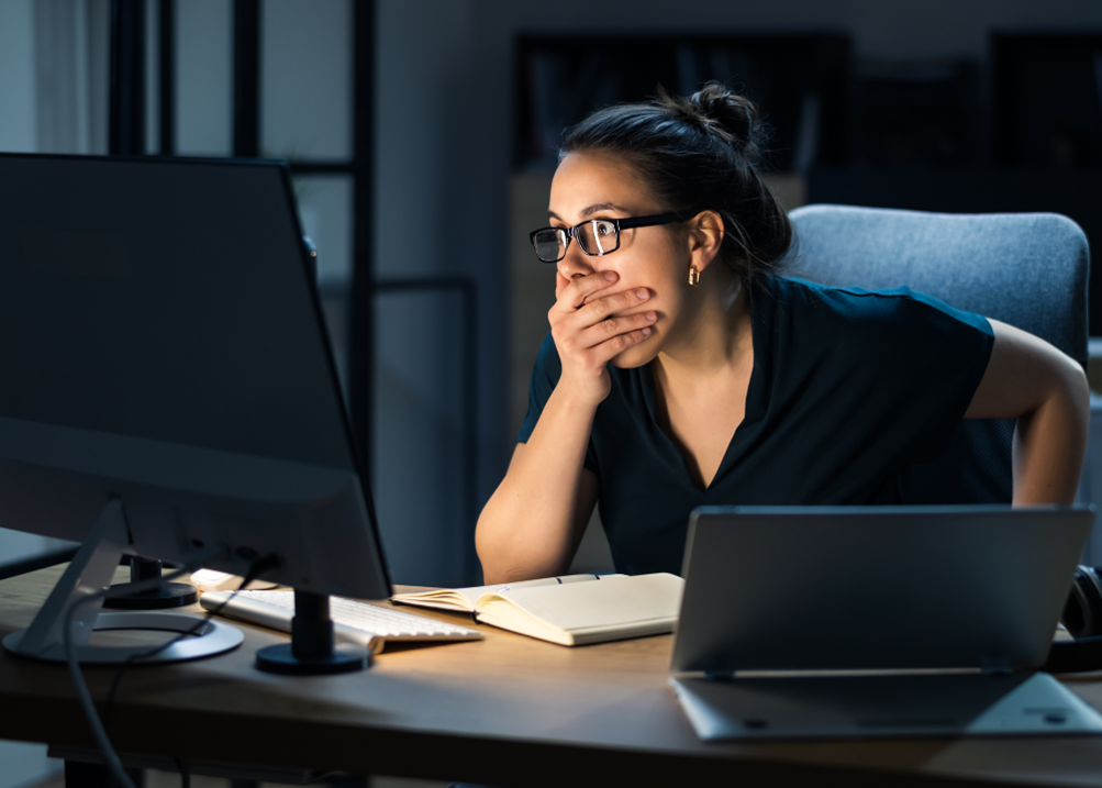 Woman sitting behind computer, looking shocked