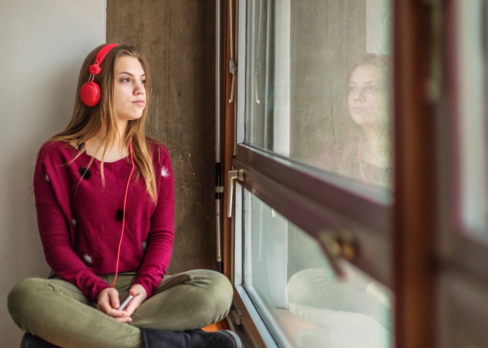 Teen wearing headphones, looking out of window